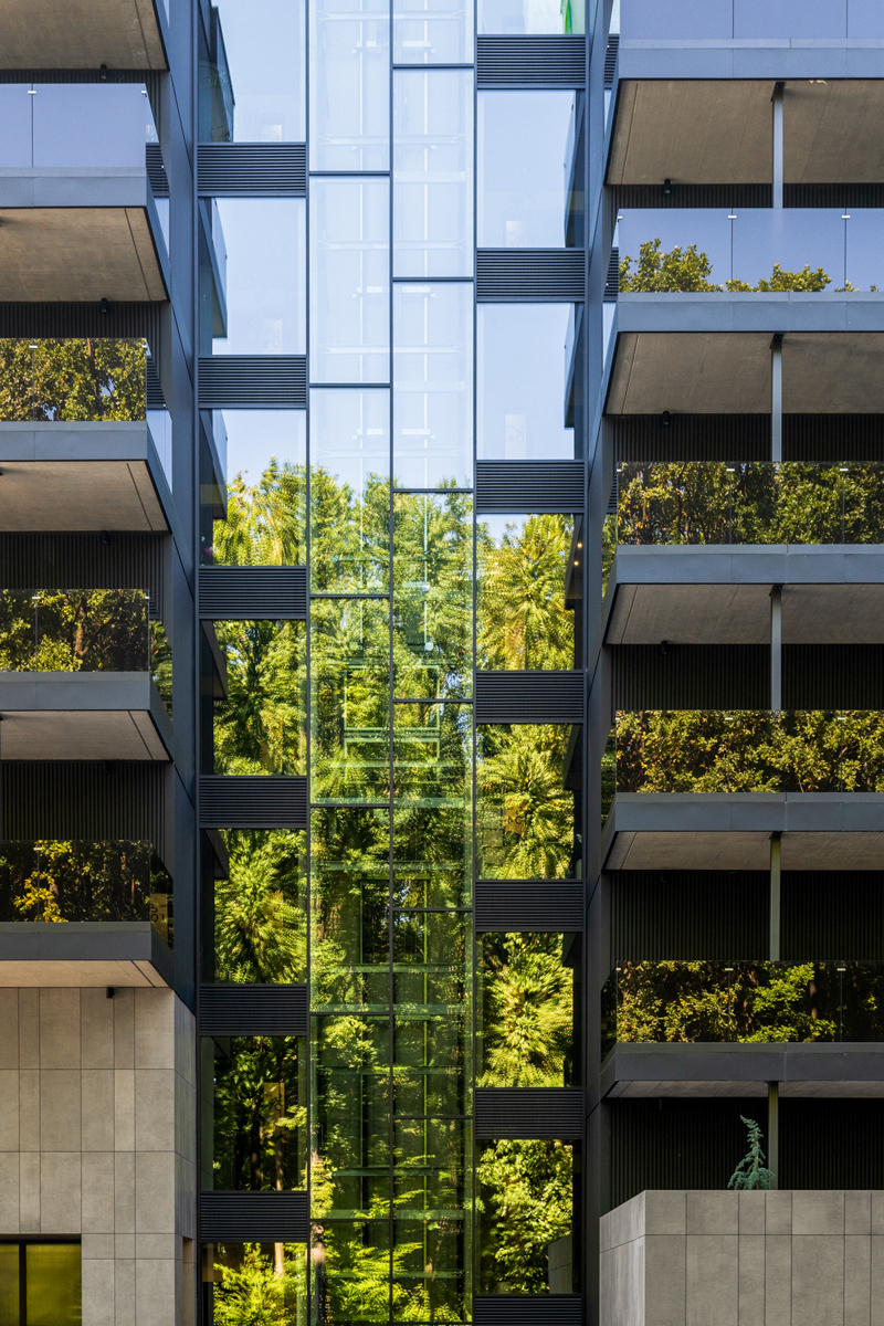 Prosklené jádro domu s výtahem, který odráží okolní zeleň a přirozené světlo.