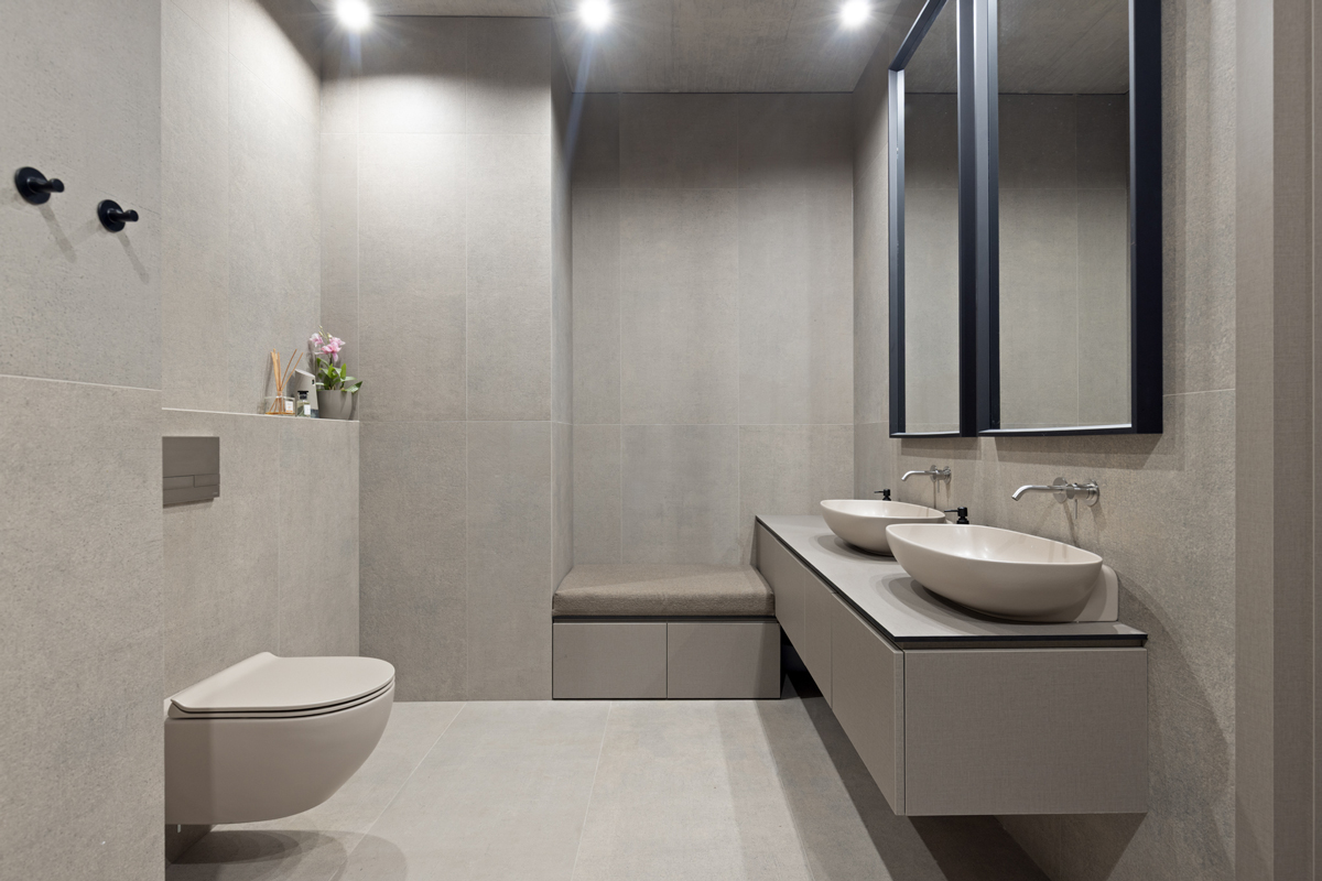 Koupelna v tlumených šedých tónech s dvojicí keramických umyvadel a závěsným WC.