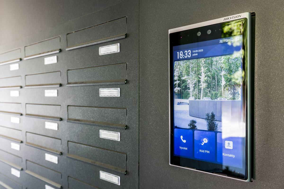 Moderní domovní systém s dotykovým displejem a integrovanou kamerou u vstupu do budovy.