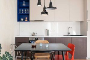 Obytný prostor propojující kuchyň, jídelní kout a obývací část s různorodými židlemi a závěsnými světly.