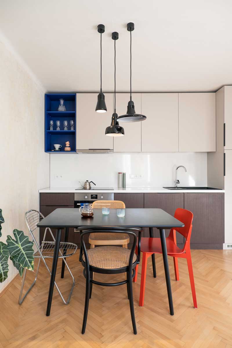 Obytný prostor propojující kuchyň, jídelní kout a obývací část s různorodými židlemi a závěsnými světly.