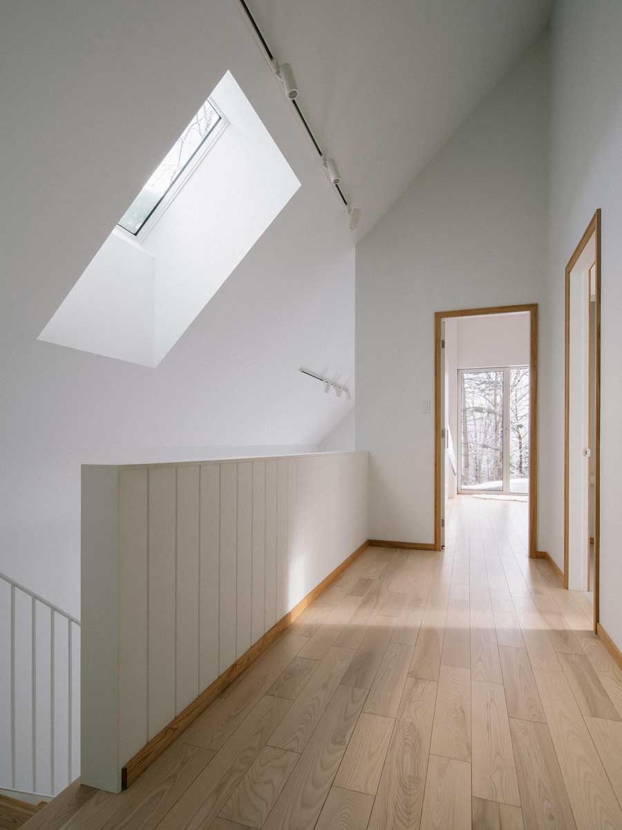 Světlá chodba dává vyniknout čistým liniím a zve pohledem ven do ticha zasněženého lesa.