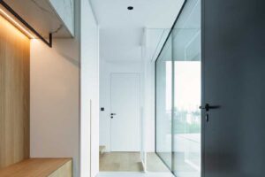 Moderní chodba s prosklenou stěnou, vestavěnou lavicí a kombinací bílých a černých prvků.