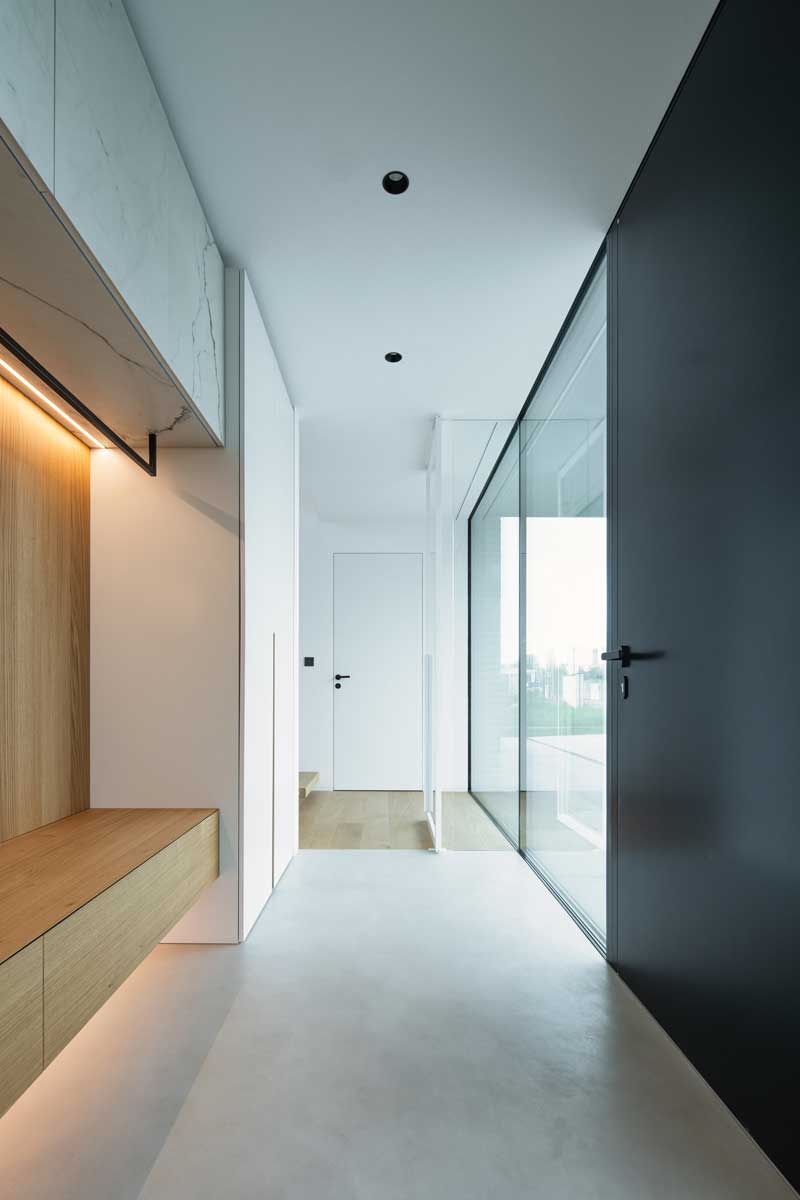 Moderní chodba s prosklenou stěnou, vestavěnou lavicí a kombinací bílých a černých prvků.