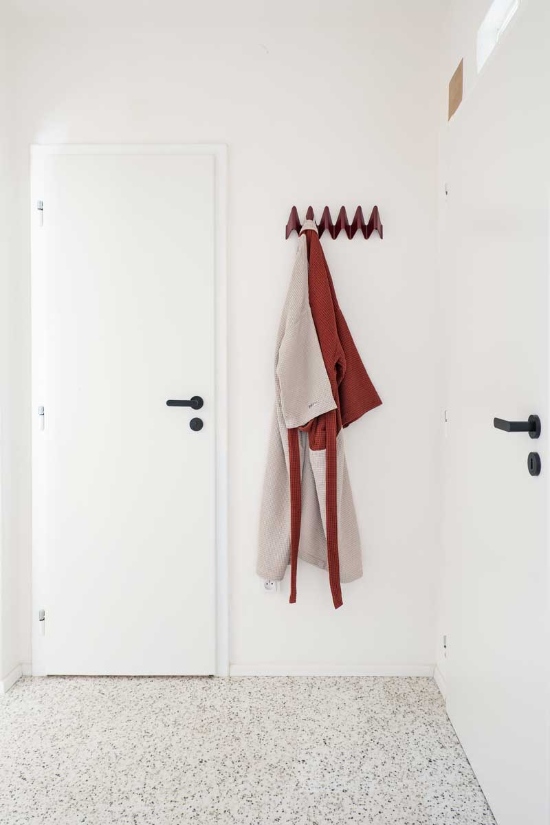 Světlá chodba s bílými dveřmi, minimalistickým věšákem a jemným terrazzo podkladem.
