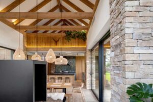 Propojení jídelny, obývacího pokoje a kuchyně v otevřeném prostoru s dřevěnými trámy a prosklením