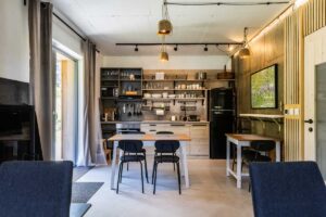 Společenská místnost chaty s kuchyní, jídelním stolem a otevřenými policemi