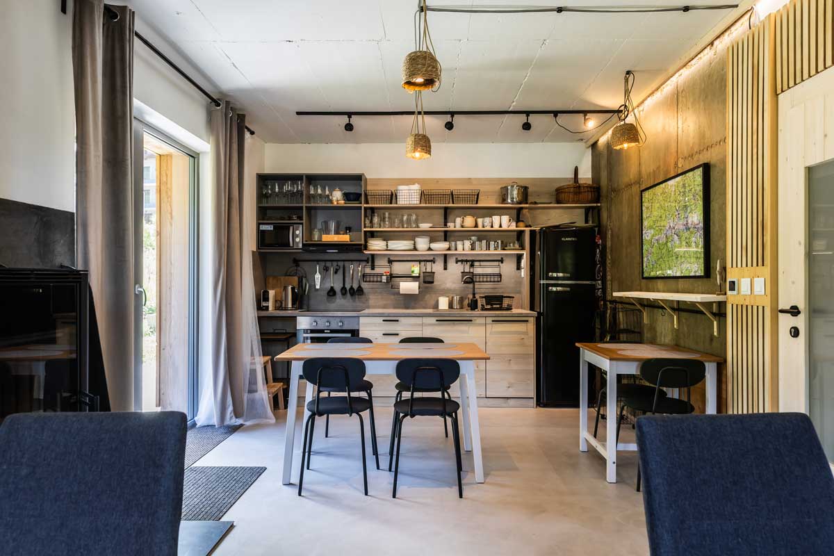 Společenská místnost chaty s kuchyní, jídelním stolem a otevřenými policemi