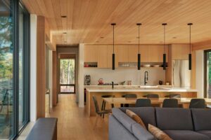 Pohled z obývacího prostoru do kuchyně s velkými prosklenými okny do lesa