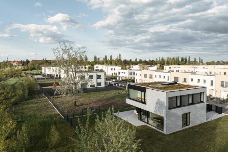 Letecký pohled na moderní rodinný dům s extenzivní zelenou střechou v rezidenční zástavbě Prahy 18.