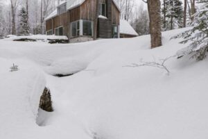 Dům vyrůstá nad zasněženým terénem u potoka a podtrhuje sílu krajiny, která ho formovala.