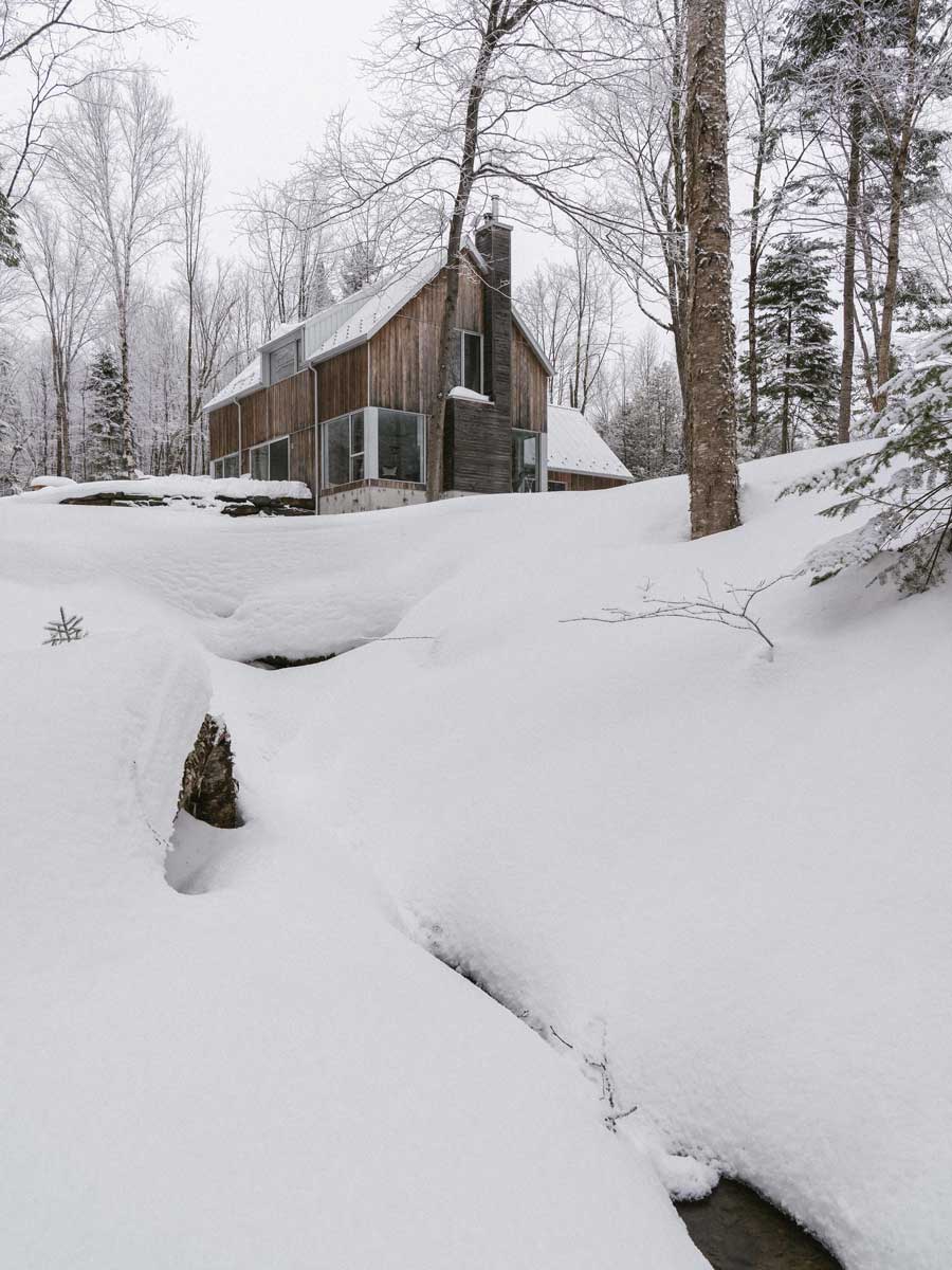 Dům vyrůstá nad zasněženým terénem u potoka a podtrhuje sílu krajiny, která ho formovala.