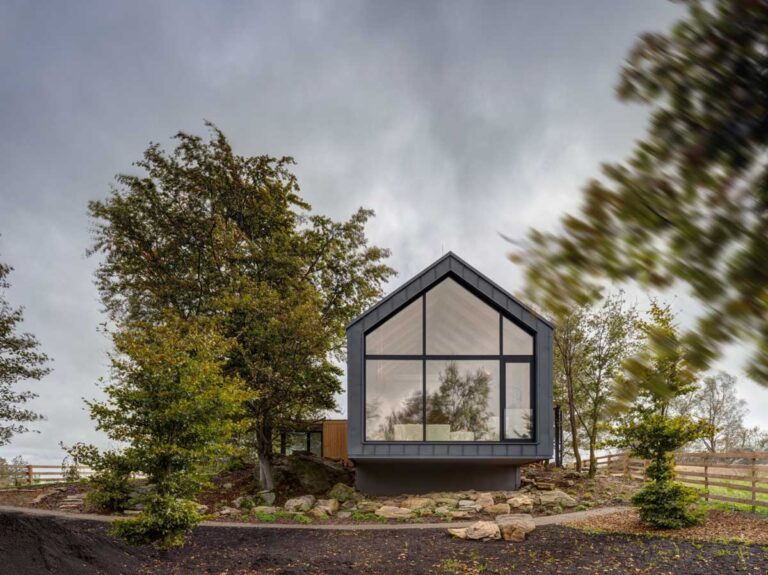 Moderní horská chata s výrazným proskleným štítem zasazená mezi stromy v podhůří Krušných hor