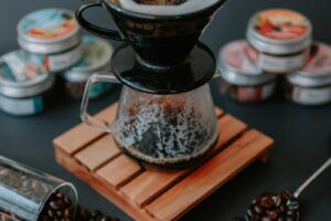 Ruční příprava kávy ve filtru s rozptýlenými zrnky kolem vytváří atmosféru pomalého ranního rituálu