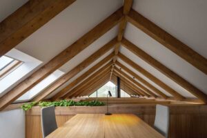 Pracovna v podkroví moderní chaty s masivními dřevěnými trámy a stolem pod šikmou střechou