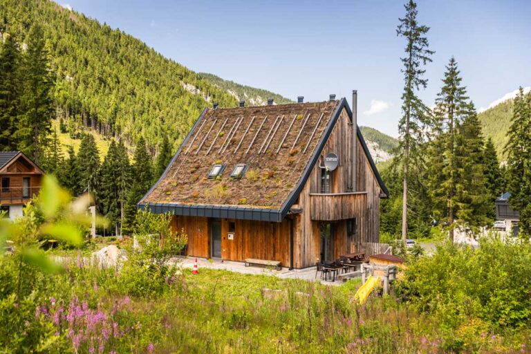 Dřevěná horská chata se zelenou střechou uprostřed horské krajiny