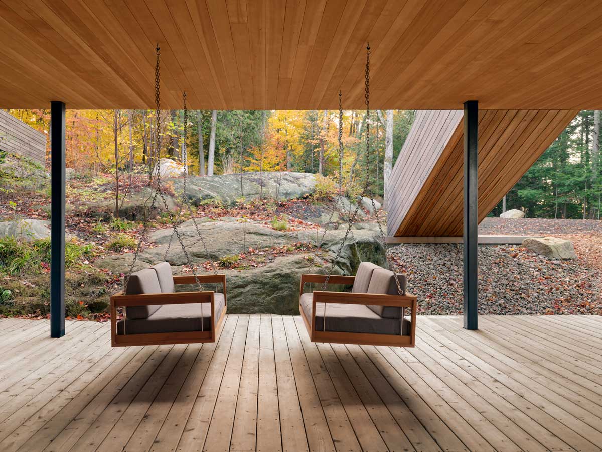 Krytá terasa s dřevěnou podlahou a závěsnými houpačkami mezi skalami