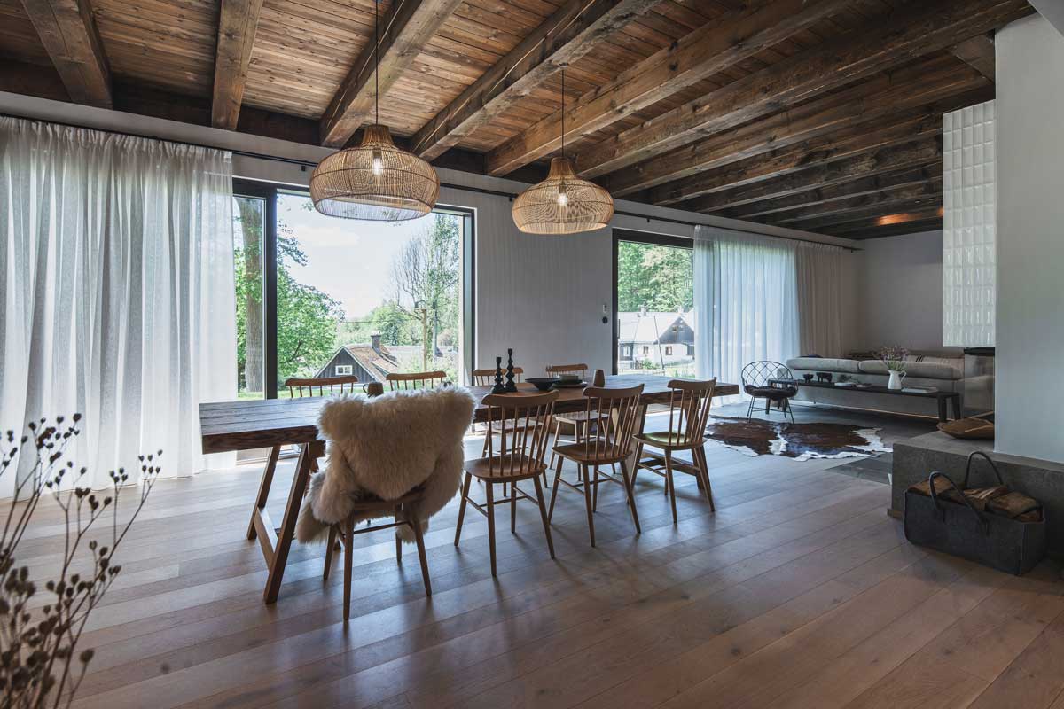 Jídelna v horské chalupě s velkým dřevěným stolem, trámovým stropem a výhledem do zahrady