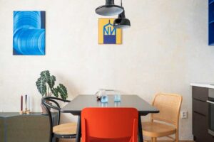 Jídelní kout v malém bytě s červenou designovou židlí, černým stolem a závěsnými svítidly.