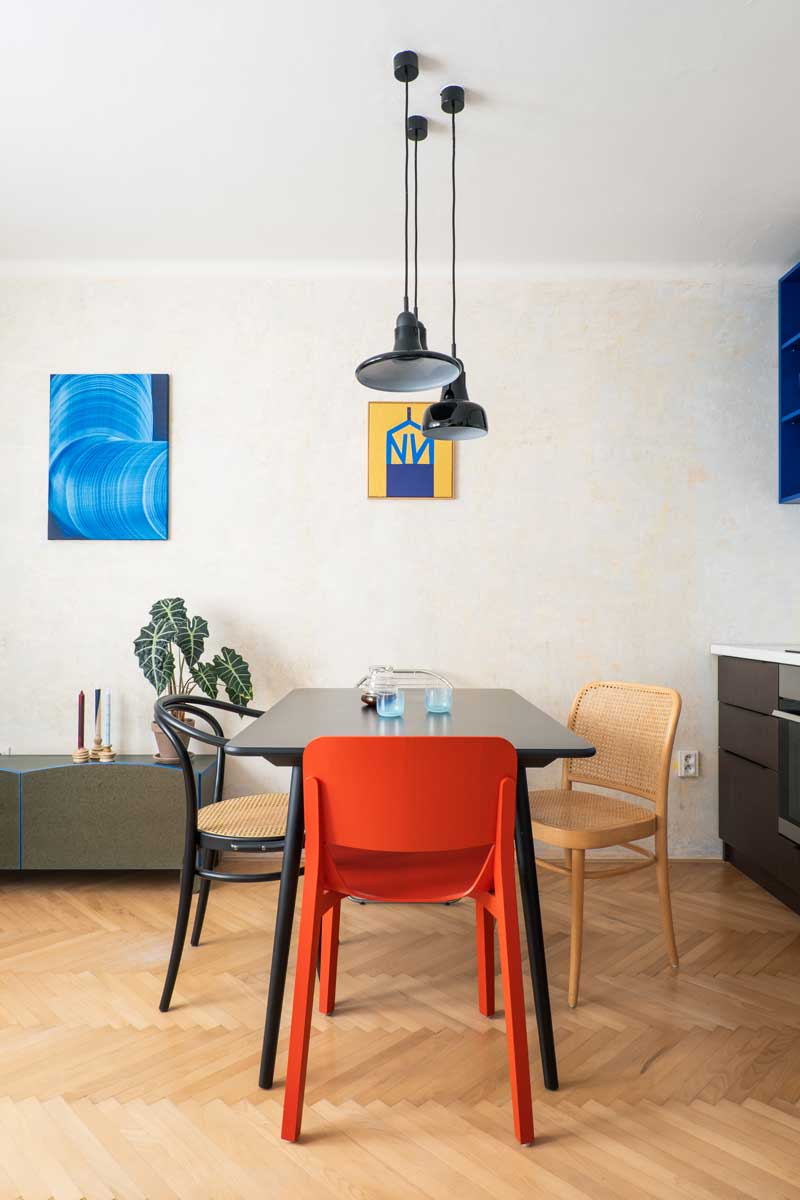 Jídelní kout v malém bytě s červenou designovou židlí, černým stolem a závěsnými svítidly.
