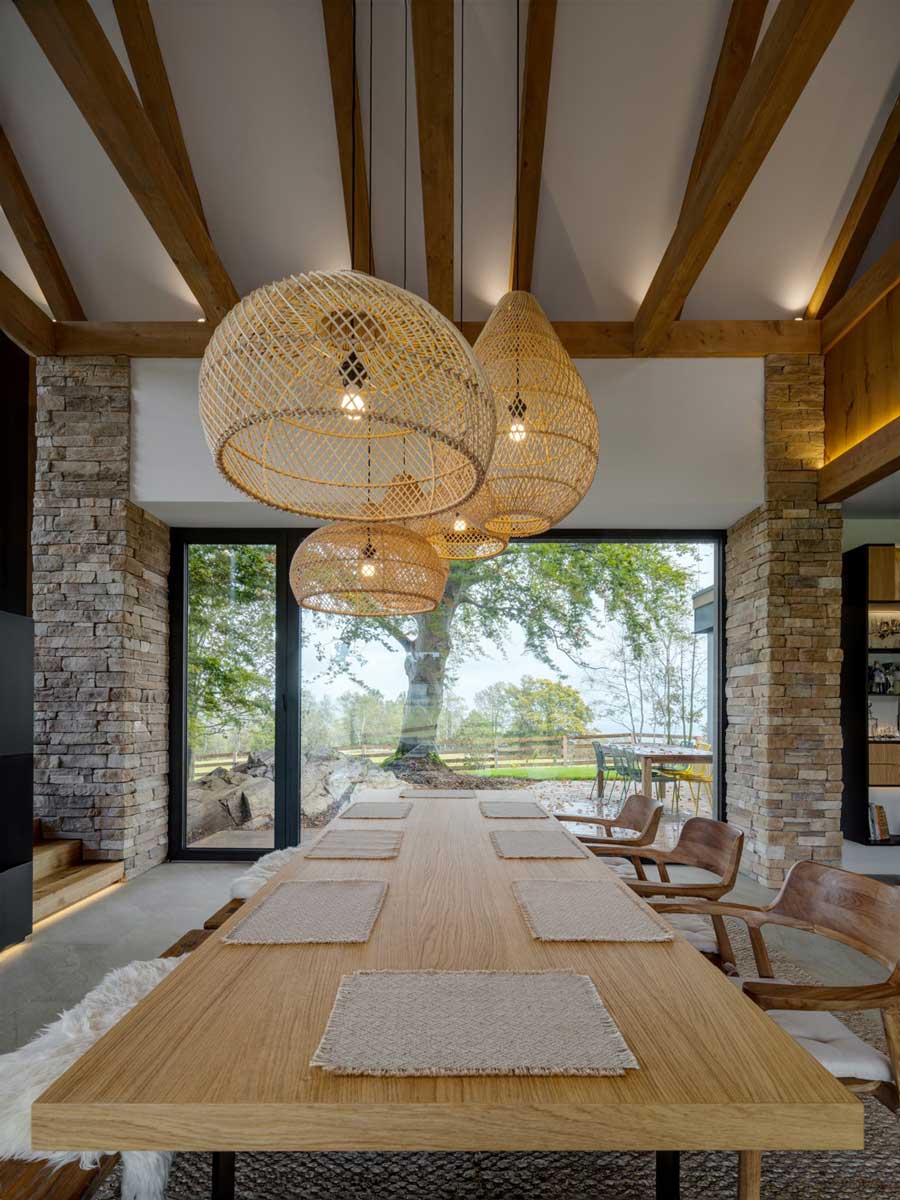 Dlouhý dřevěný jídelní stůl s ratanovými závěsnými lampami v centrální části moderní chaty