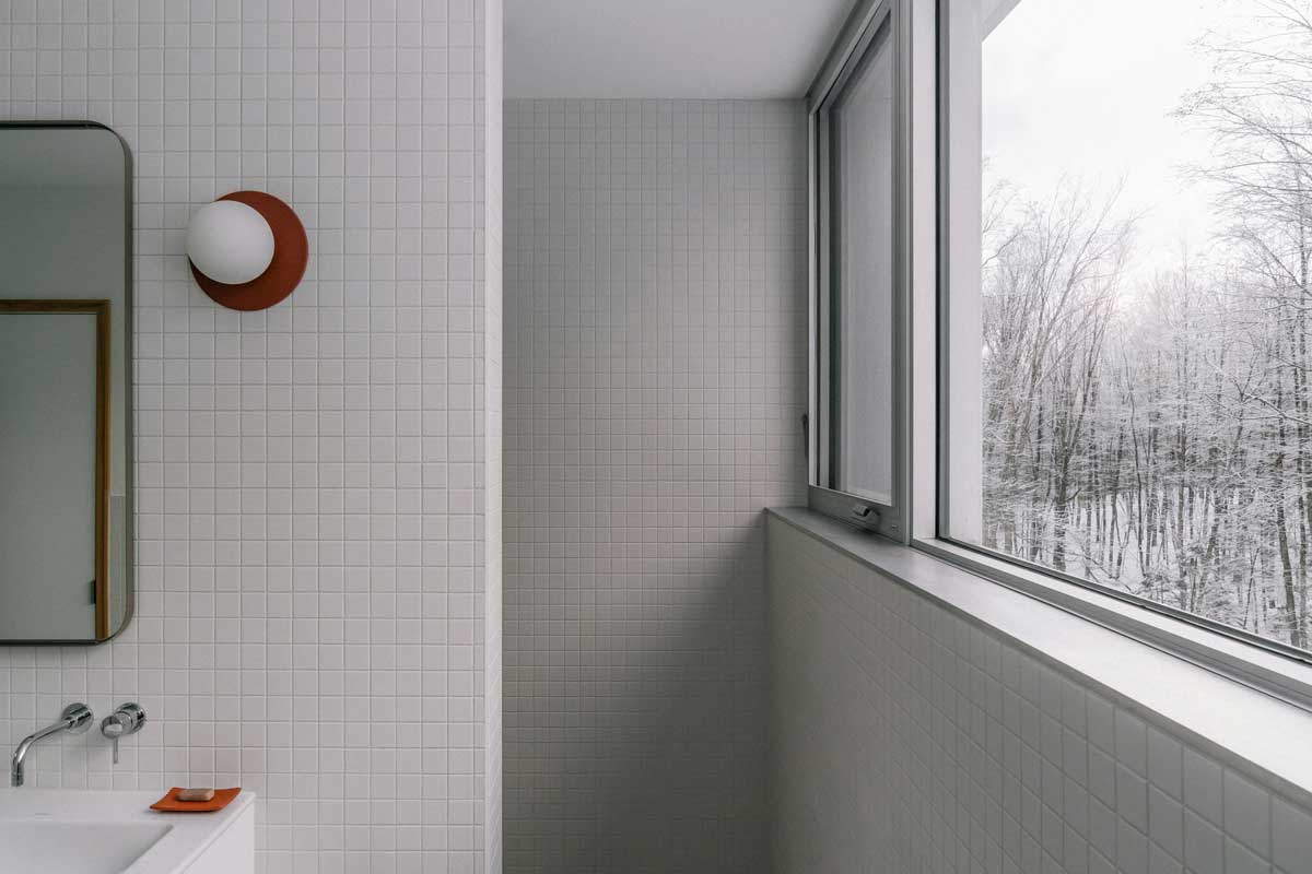 Minimalistická koupelna otevírá intimní pohled do zimní krajiny a zdůrazňuje klid celého domu.