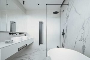 Luxusní koupelna s mramorovými obklady, volně stojící vanou a černými vodovodními bateriemi.