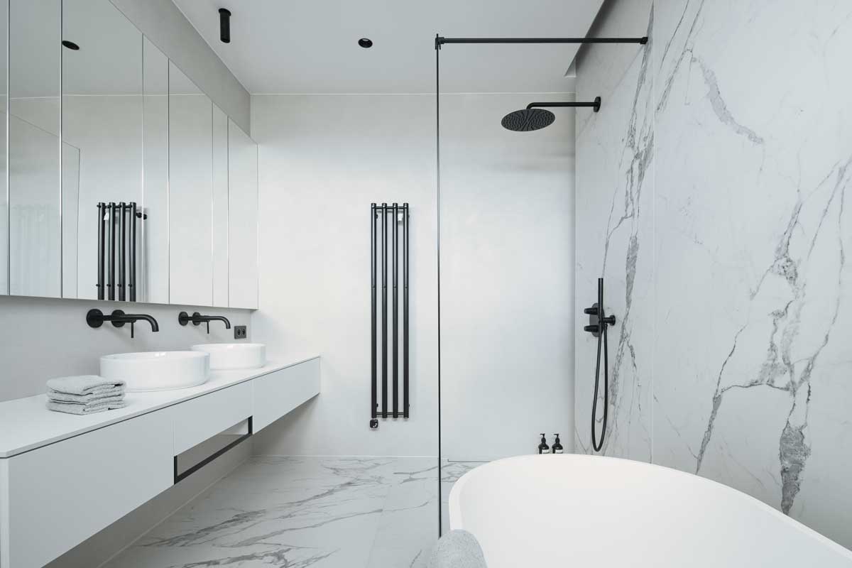 Luxusní koupelna s mramorovými obklady, volně stojící vanou a černými vodovodními bateriemi.