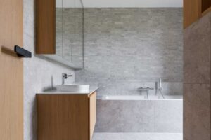 Minimalistická koupelna s vanou, kamenným obkladem a dřevěnou skříňkou na míru