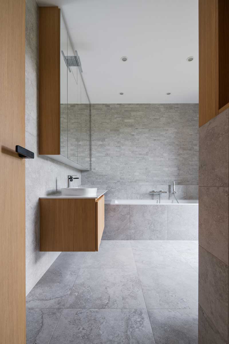 Minimalistická koupelna s vanou, kamenným obkladem a dřevěnou skříňkou na míru