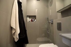 Šedá koupelna garsonky se sprchovým koutem, vestavnými skříňkami a zrcadlem.