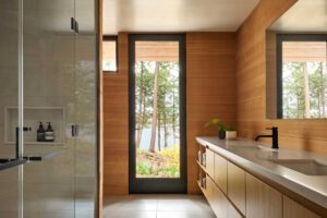 Koupelna s dřevěným obkladem a výhledem do lesa skrze prosklené dveře