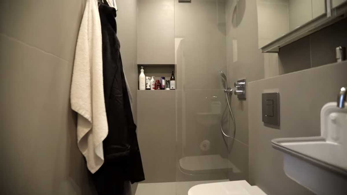 Šedá koupelna garsonky se sprchovým koutem, vestavnými skříňkami a zrcadlem.