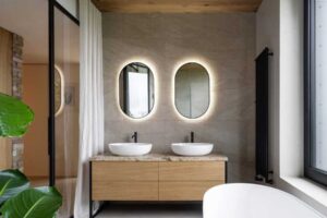 Elegantní koupelna se dvěma umyvadly, podsvícenými oválnými zrcadly a přírodním kamenem.