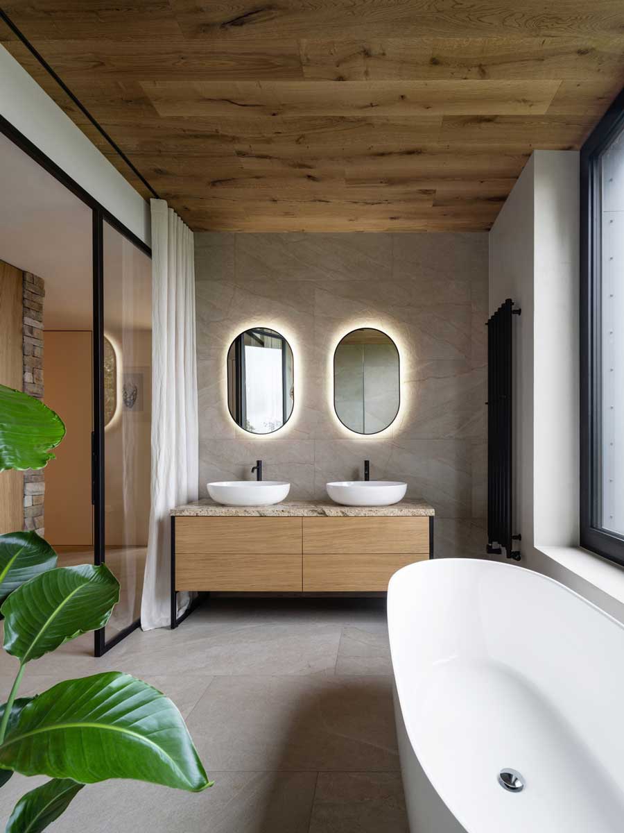 Elegantní koupelna se dvěma umyvadly, podsvícenými oválnými zrcadly a přírodním kamenem.