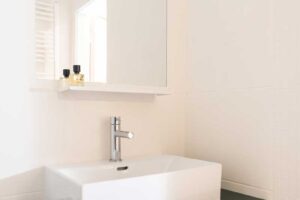 Minimalistická koupelna s černomodrou umyvadlovou skříňkou a velkým zrcadlem.