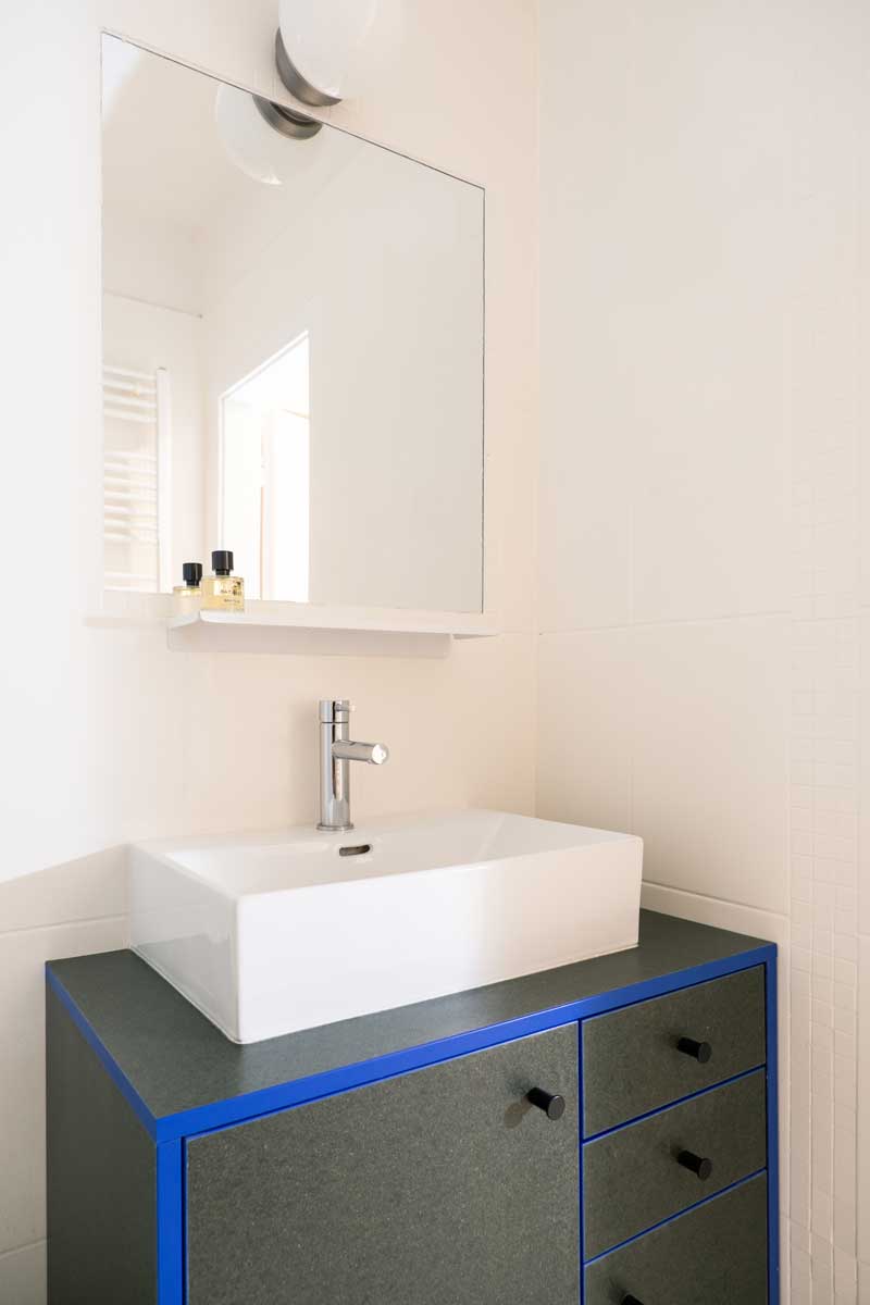 Minimalistická koupelna s černomodrou umyvadlovou skříňkou a velkým zrcadlem.