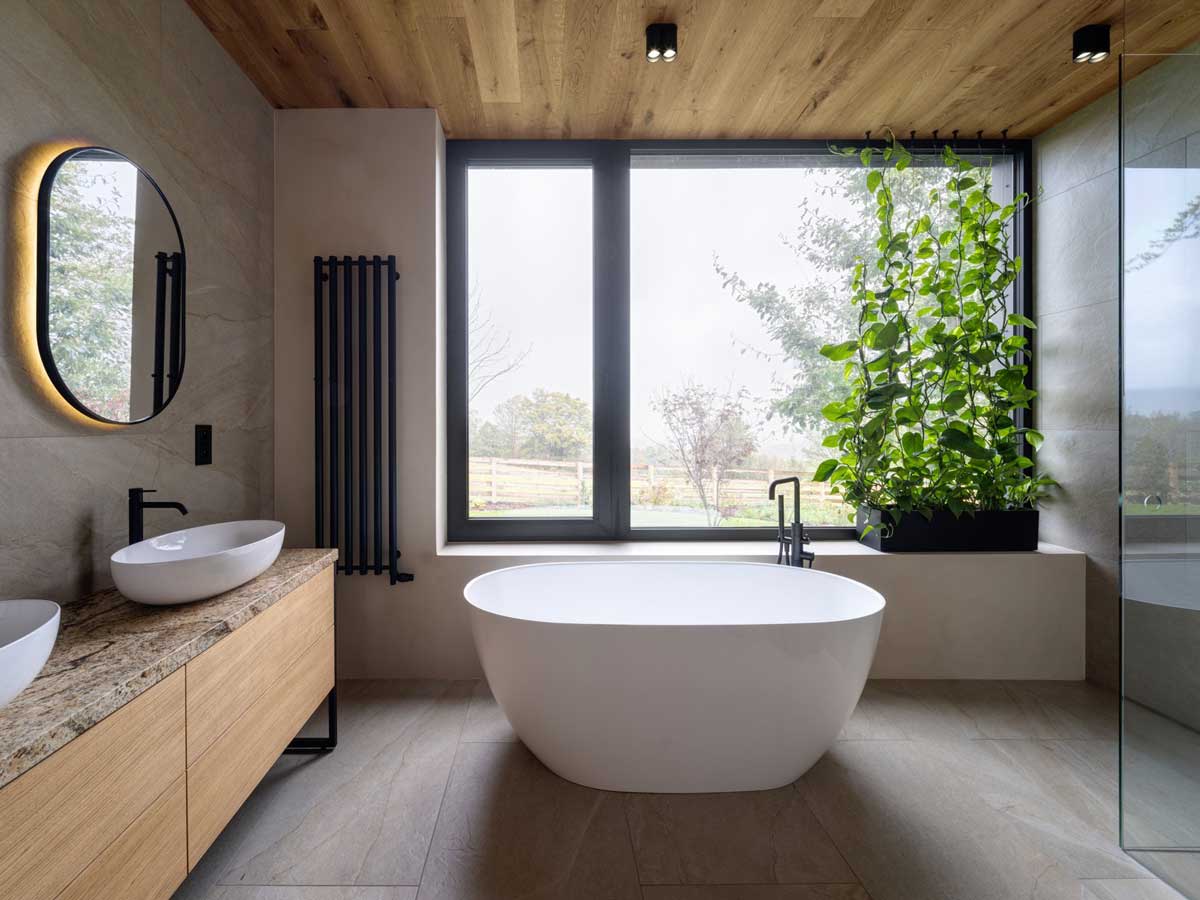Koupelna s volně stojící vanou u velkého okna a zelení, která dotváří atmosféru.