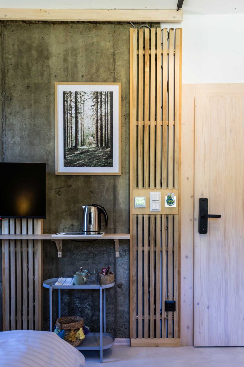 Detail interiéru chaty s betonovou stěnou, dřevěnými lamelami a koutem s rychlovarnou konvicí