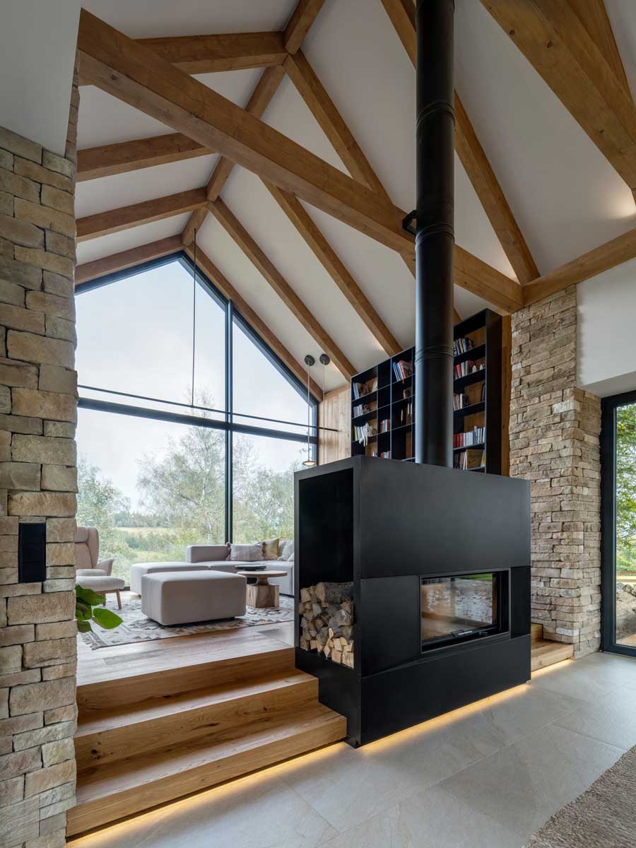 Obytný prostor s dominantním krbem, dřevěnými stropy a velkým prosklením.