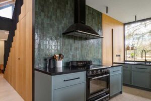 Moderní kuchyň s dřevěnými plochami, černými detaily a tmavě zeleným keramickým obkladem.