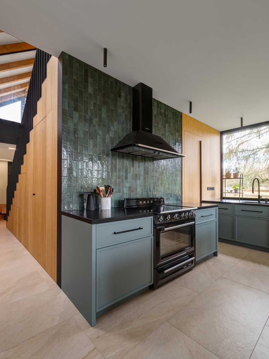 Moderní kuchyň s dřevěnými plochami, černými detaily a tmavě zeleným keramickým obkladem.