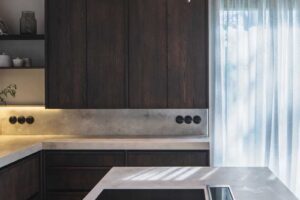 Kuchyně s tmavým dřevem, kamennou deskou a trámovým stropem v moderní horské chalupě