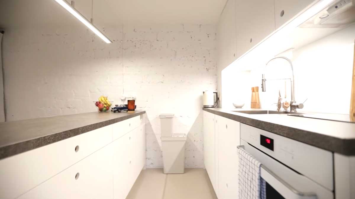 Světlá garsonková kuchyně s bílými skříňkami, hlubokými zásuvkami a tmavou pracovní deskou.