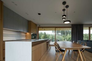 Propojený prostor kuchyně a jídelny s velkým stolem a výhledem do zeleně