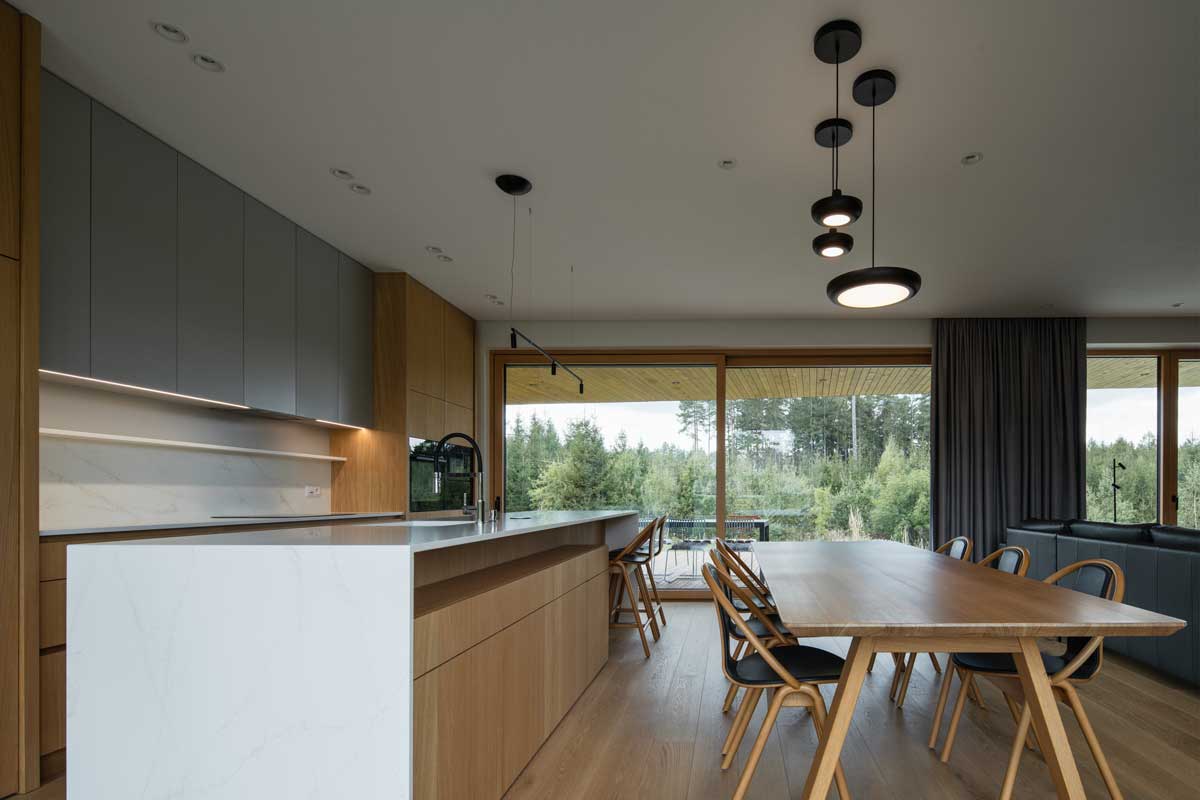 Propojený prostor kuchyně a jídelny s velkým stolem a výhledem do zeleně