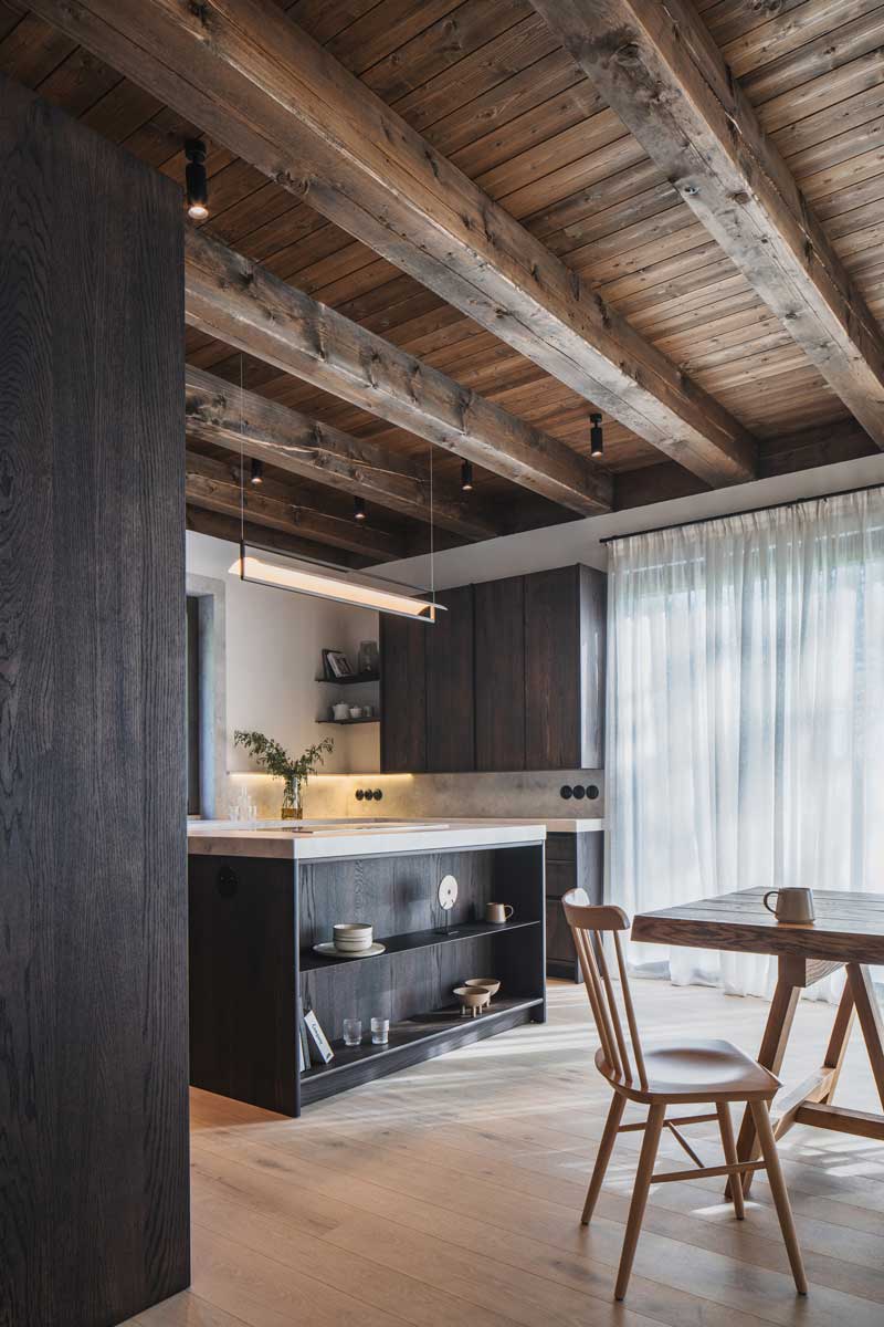 Otevřený prostor kuchyně a jídelny s velkým stolem a dřevěnými trámy