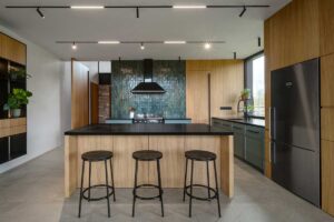 Prostorná kuchyň s velkým ostrůvkem, barovými židlemi a výraznou zelenou dlažbou na stěně.