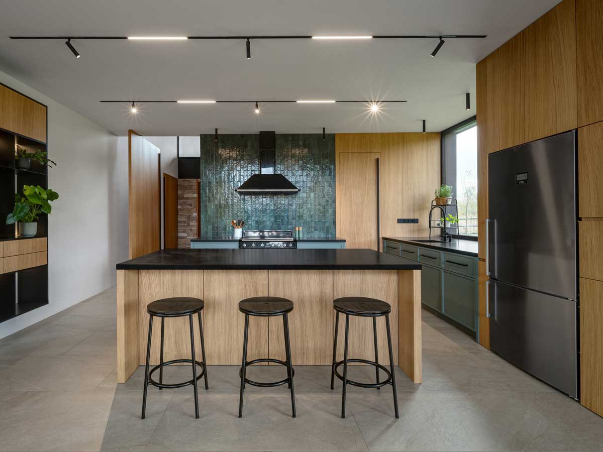 Prostorná kuchyň s velkým ostrůvkem, barovými židlemi a výraznou zelenou dlažbou na stěně.