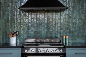 Detail černého sporáku SMEG umístěného před lesklým zeleným keramickým obkladem.